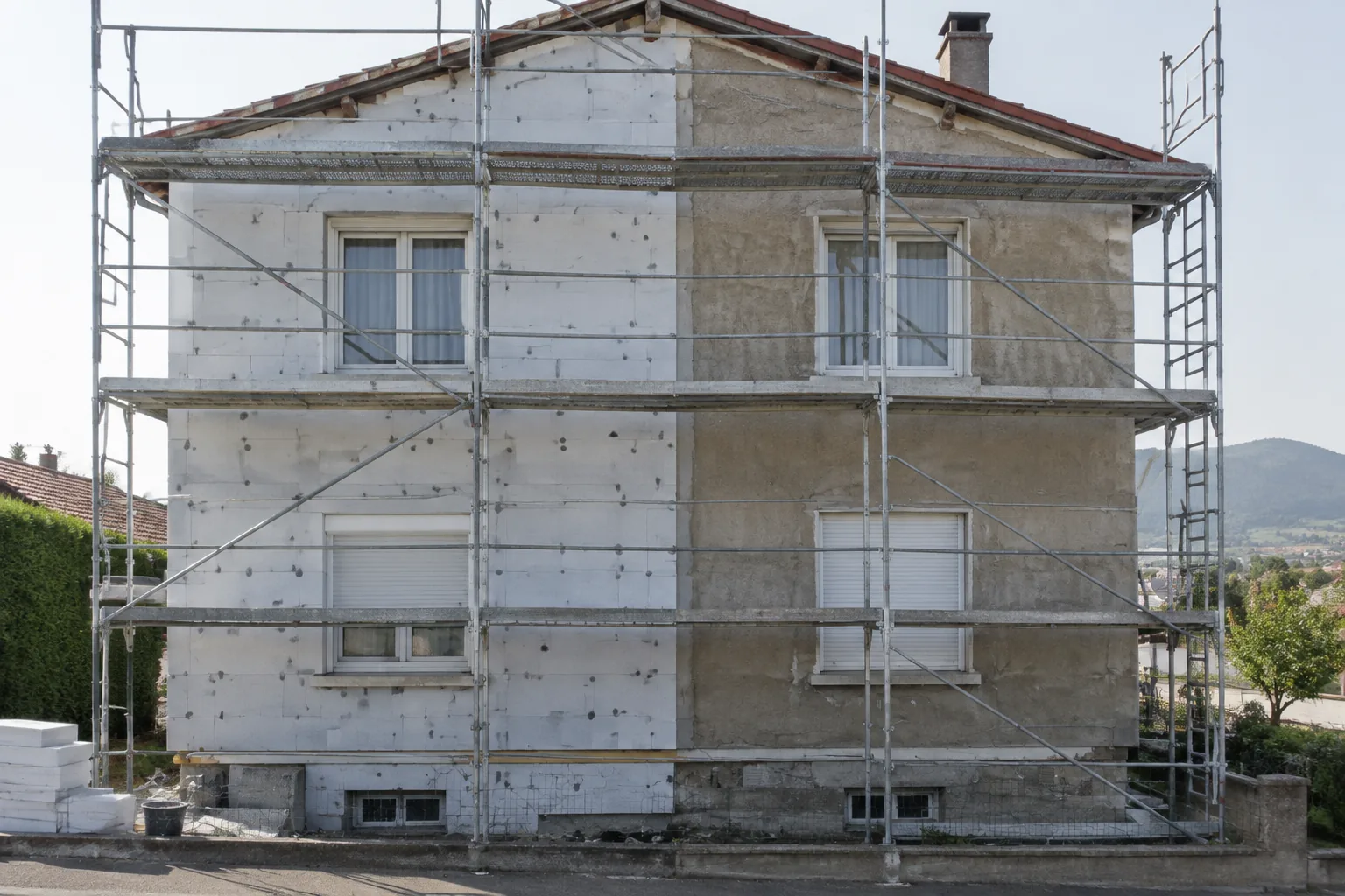 Façade sous échafaudage, une moitié déjà couverte de panneaux isolants, l'autre en enduit nu